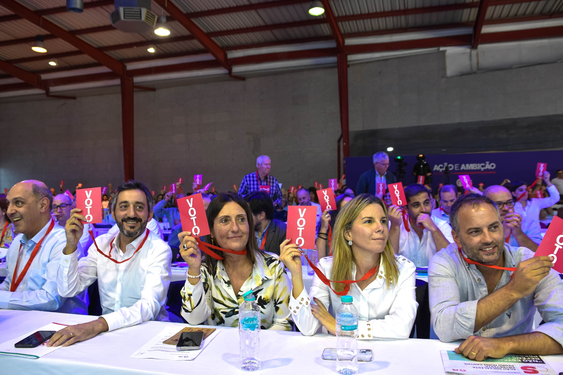 Participantes no congresso a votar com cartões vermelhos erguidos.