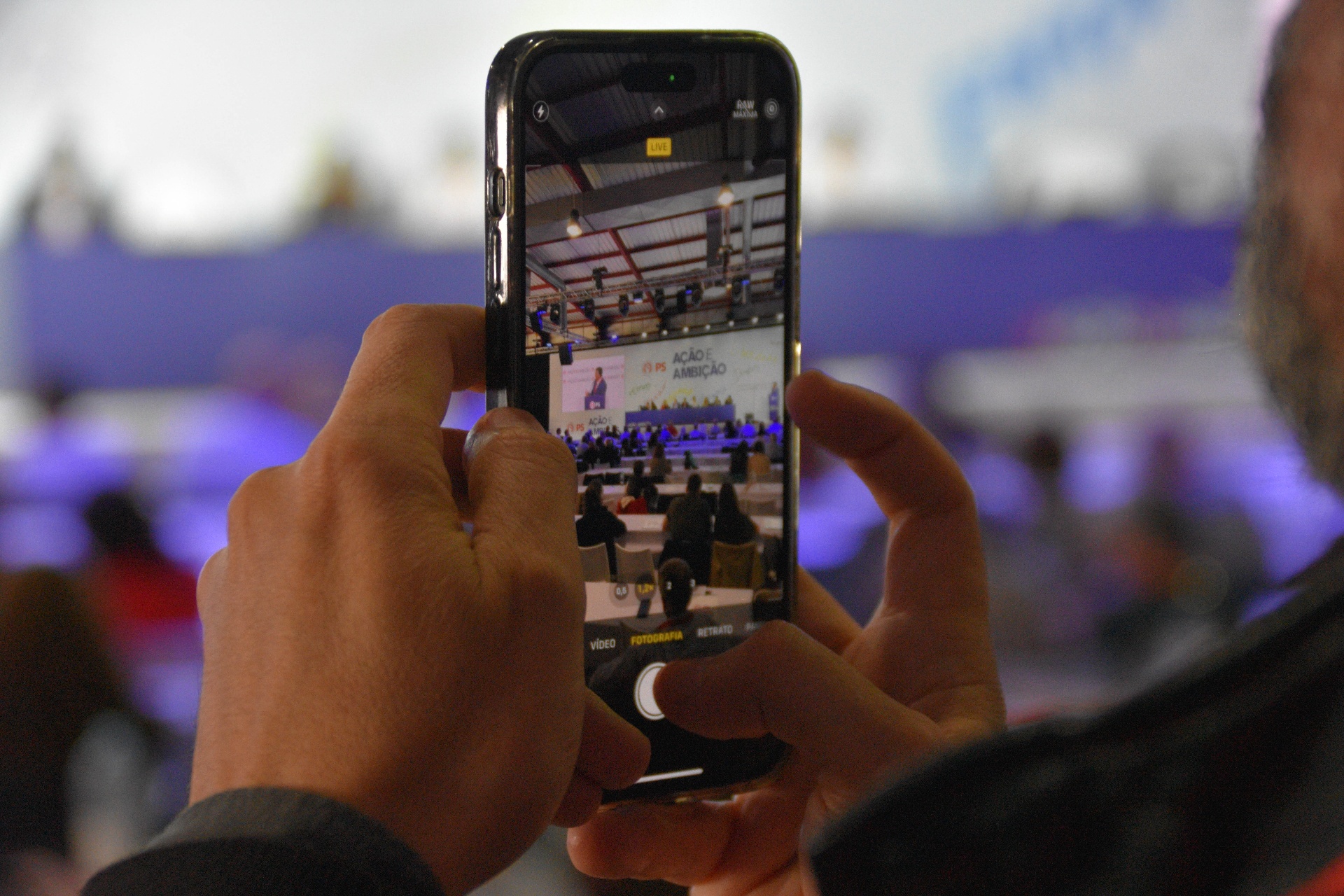Pessoa a fotografar o palco do congresso com telemóvel em primeiro plano.