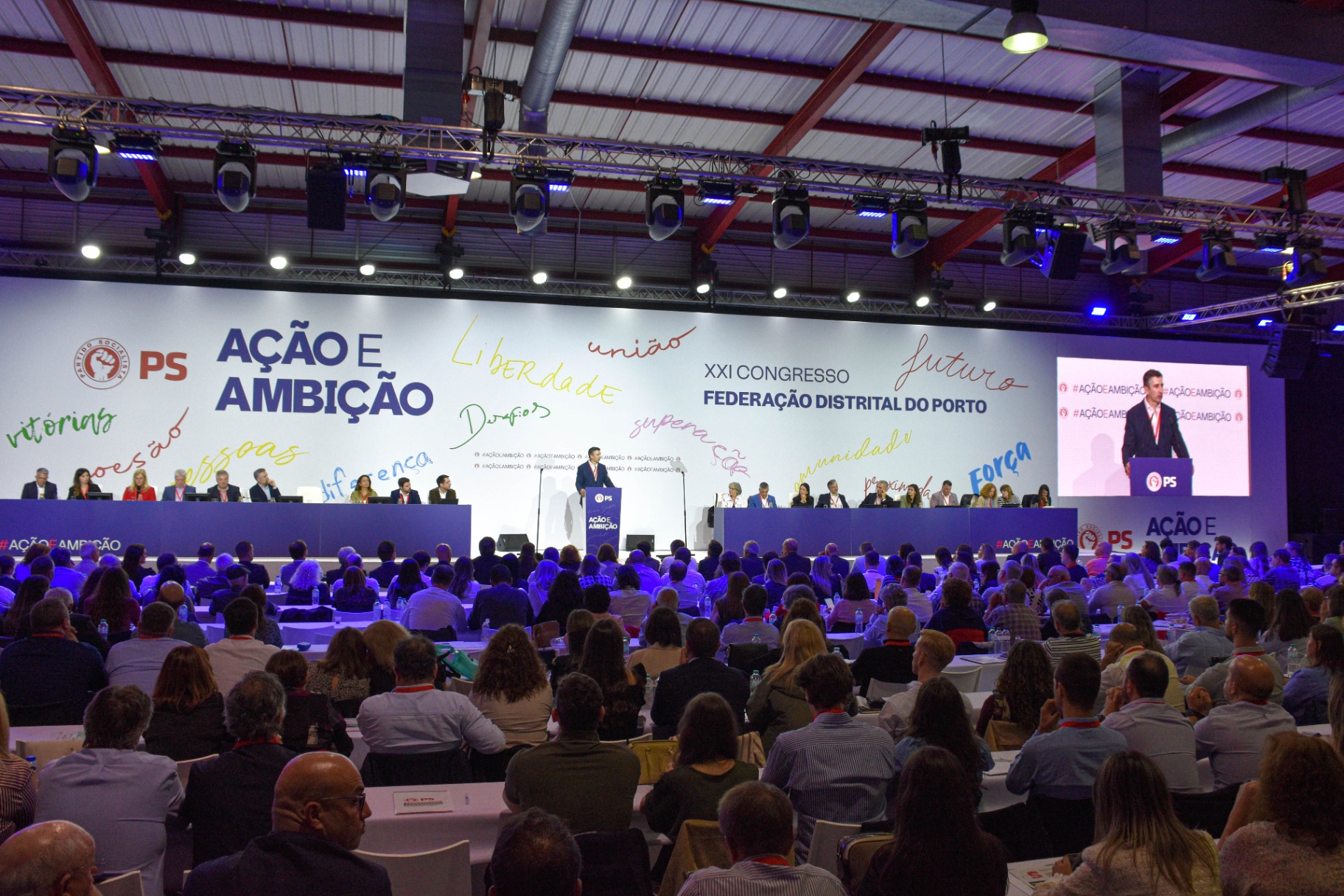 Vista geral do palco principal com intervenção perante auditório cheio.