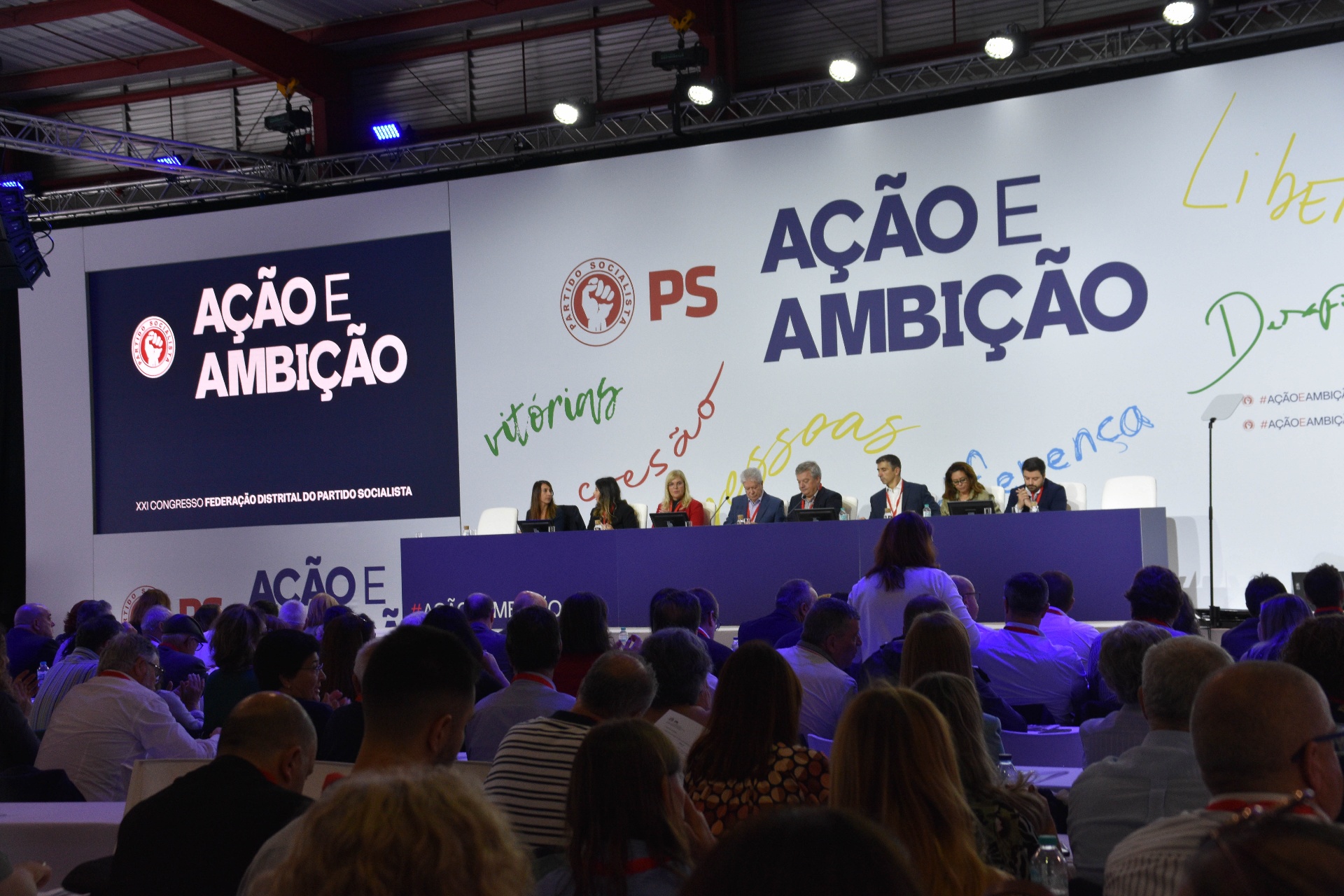 Palco do congresso com identidade visual Ação e Ambição em destaque.