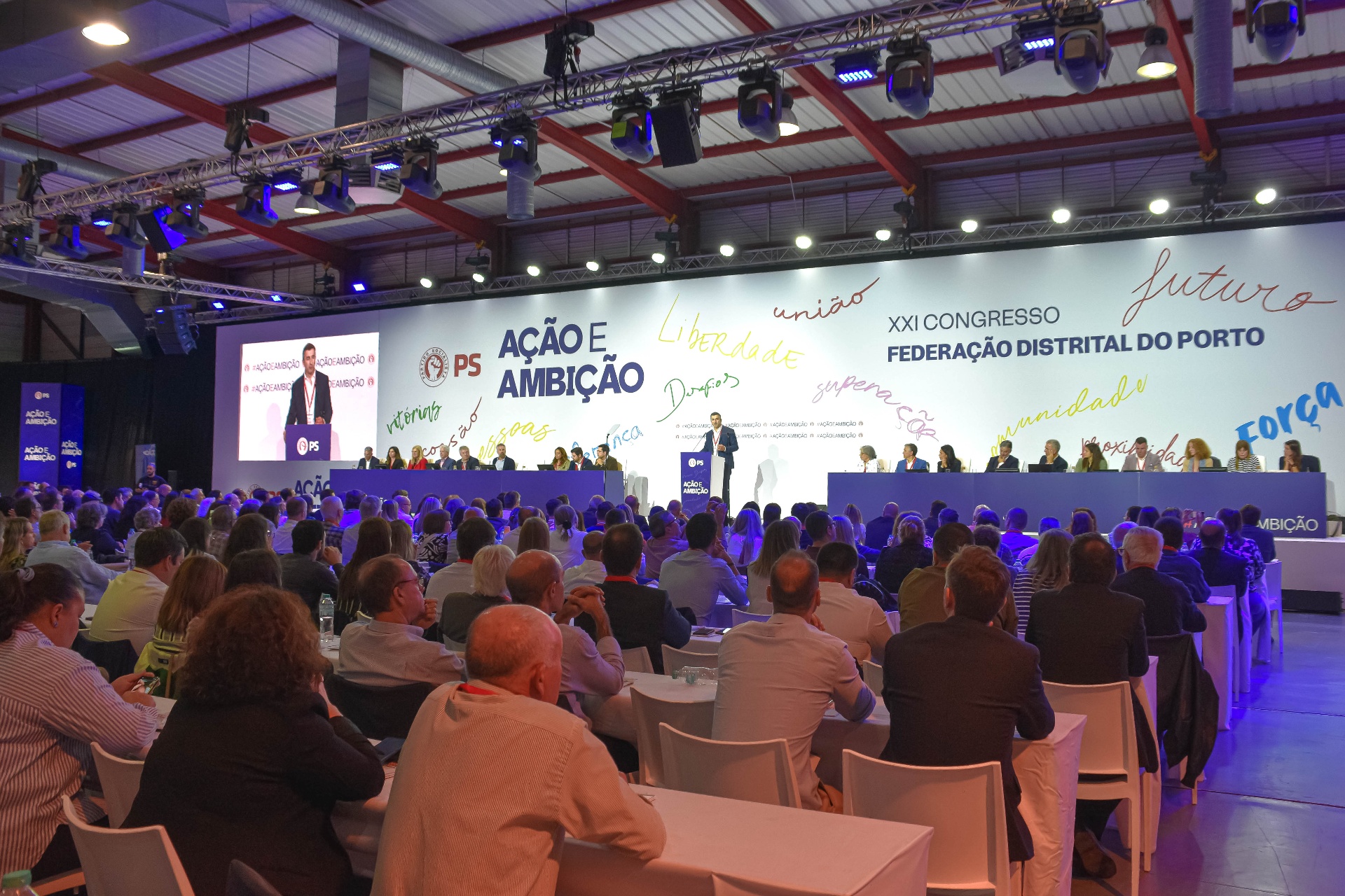 Panorâmica da sessão plenária com palco, plateia e identidade visual do congresso.