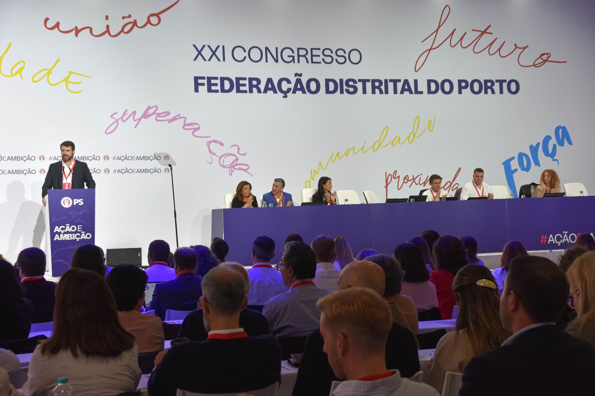 Orador no palco do congresso distrital do Porto com plateia em primeiro plano.